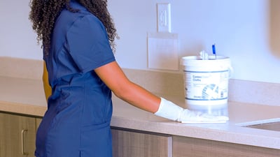 nurse in navy scrubs wiping down tan counter